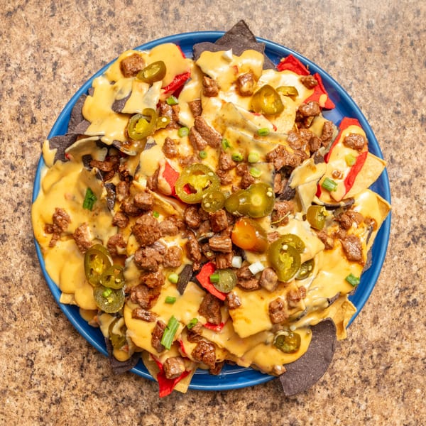 Overhead view of a blue plate piled high with nachos, cheese, meat, and jalapeños.