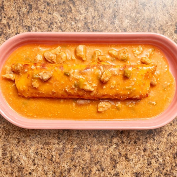 A large burrito covered in orange sauce with chunks of meat, served in a pink dish.