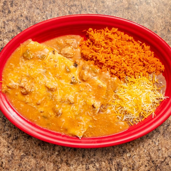 Red oval plate with enchiladas covered in cheese sauce, orange rice, and refried beans.