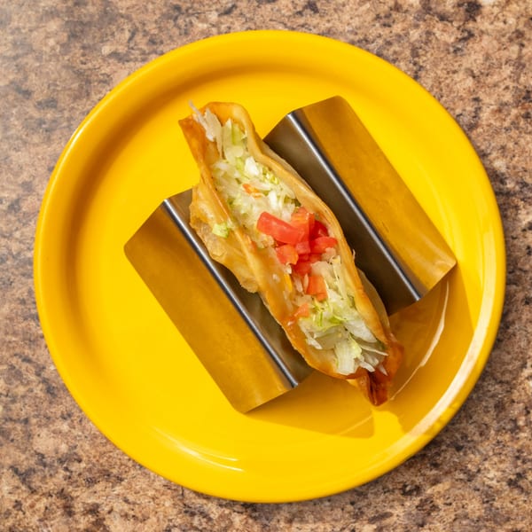 A crispy taco filled with shredded lettuce and diced tomatoes, served in a metal holder on a yellow plate.