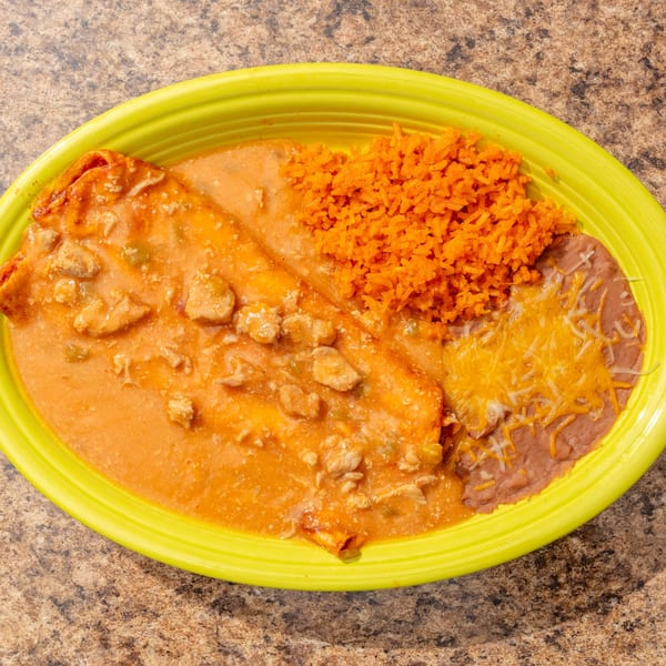 Chicken enchilada with red sauce, rice, and refried beans with cheese on a lime green plate.