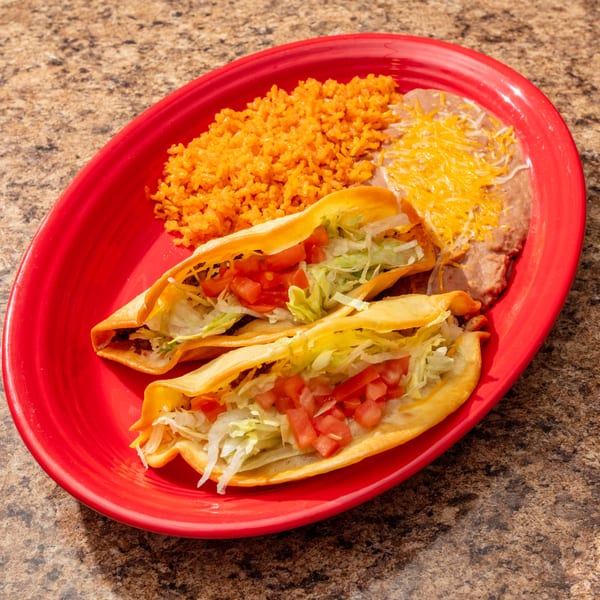 Two crispy tacos with lettuce and tomatoes, served with rice and refried beans on a red plate.