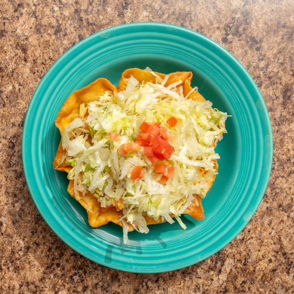 A taco salad in a crispy fried tortilla bowl, topped with shredded lettuce and diced tomatoes.